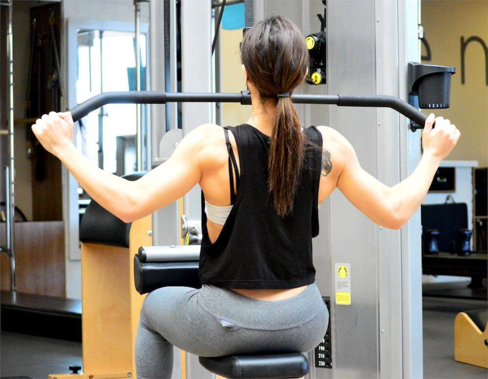 Woman pulling on a bar of weight lifting machine.