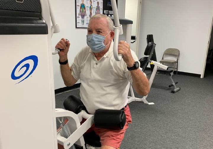 older adult man using pulldown strength training machine while wearing mask