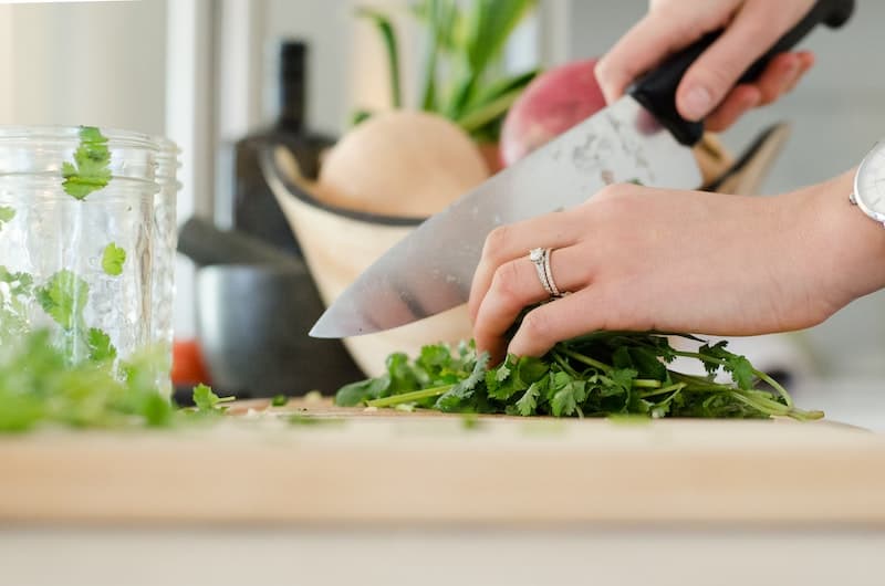 close up of hands using knife to dice herbs on cutting board