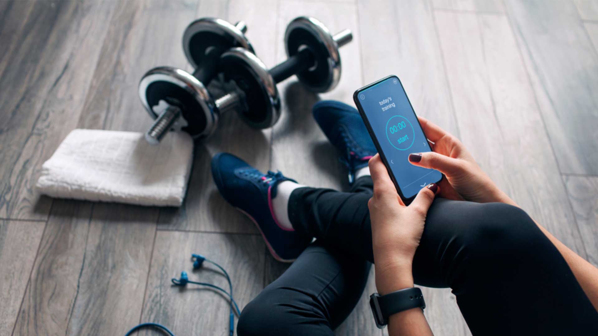 Woman sitting on the floor of a gym looking at her cell phone