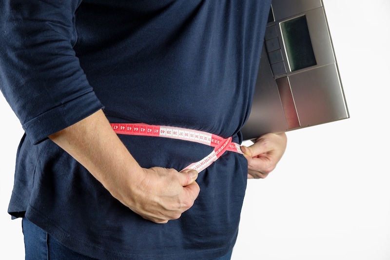 man wearing t-shirt and holding tape measure around belly