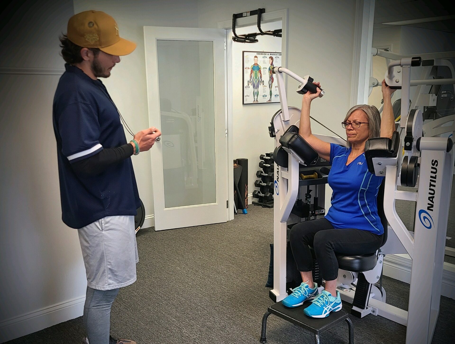certified personal trainer observes woman using strength training machine