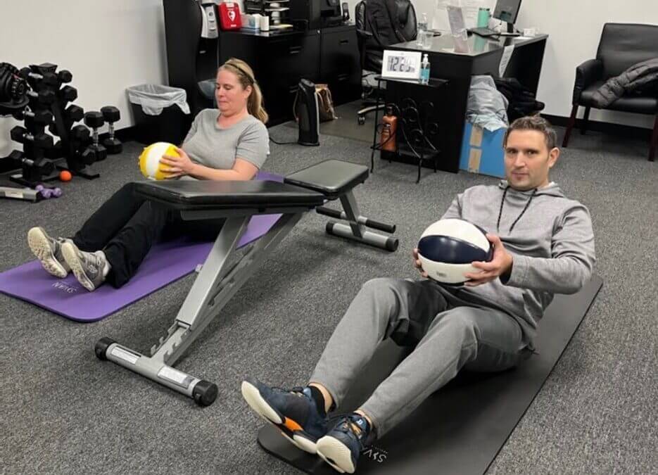 Two people doing strength training exercises at Loyalty Fitness with weighted medicine balls
