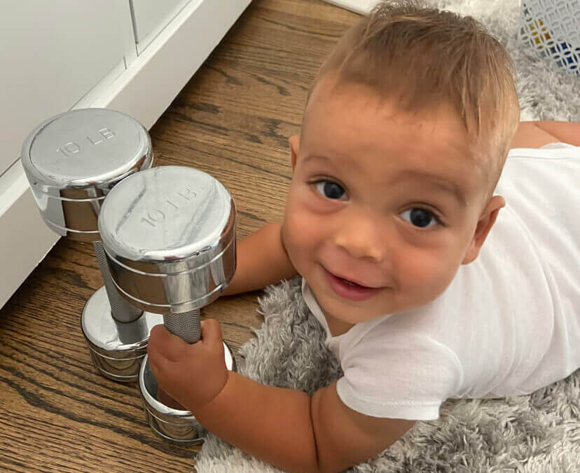 A baby laying on a rug on a floor clutching two small weights