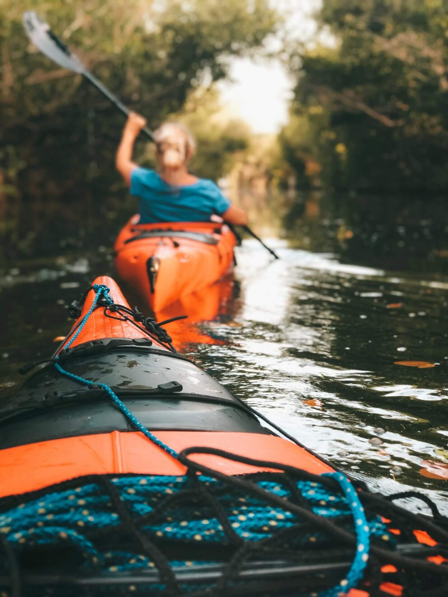 Person on a kayak behind another person kayaking with trees surrounding the lake.