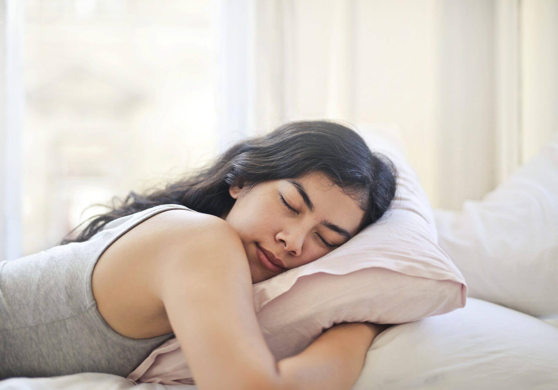 Woman sleeping with her face to the side while hugging a pillow.