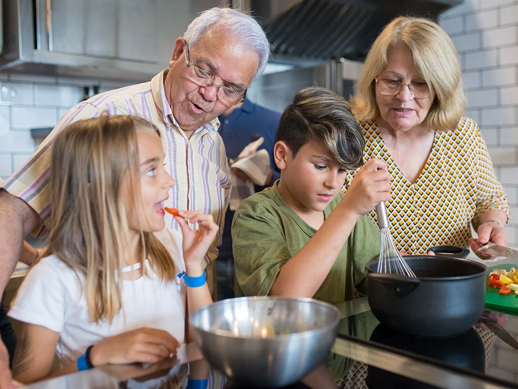 Grandparents in the kitchen with grandchildren, teaching them how to cook
