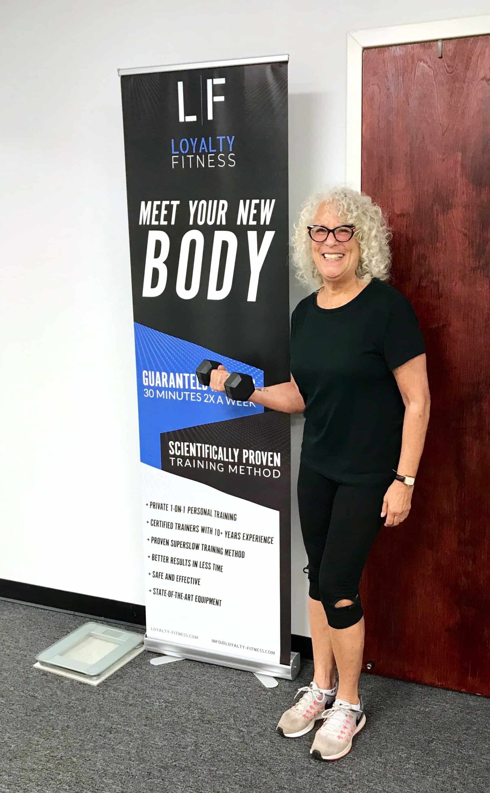 Woman holding a weight standing in front of a Loyalty Fitness sign. 