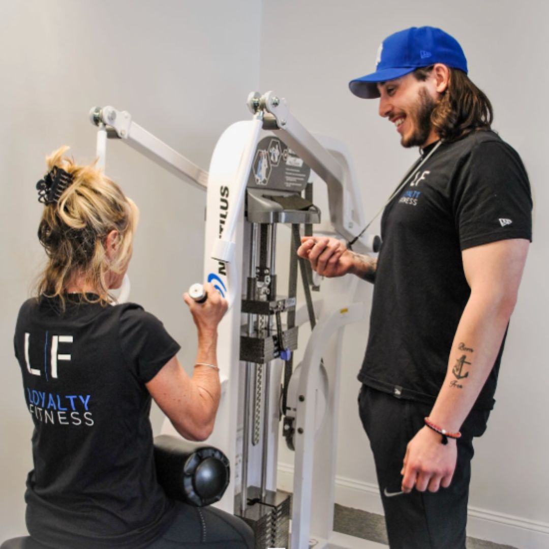 Woman training on an exercise machine with a man watching her while holding a stopwatch.