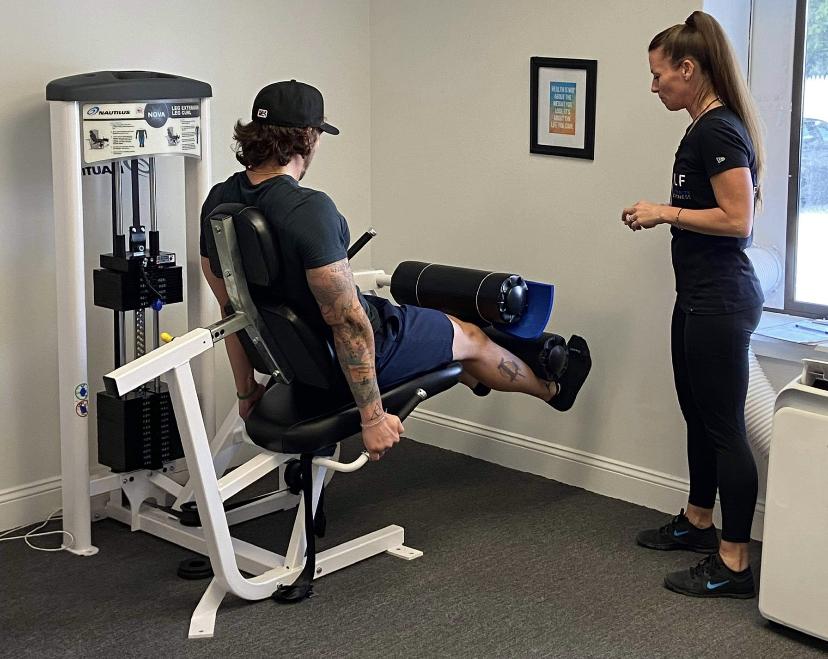 Man on a workout machine with his trainer standing right next to him.