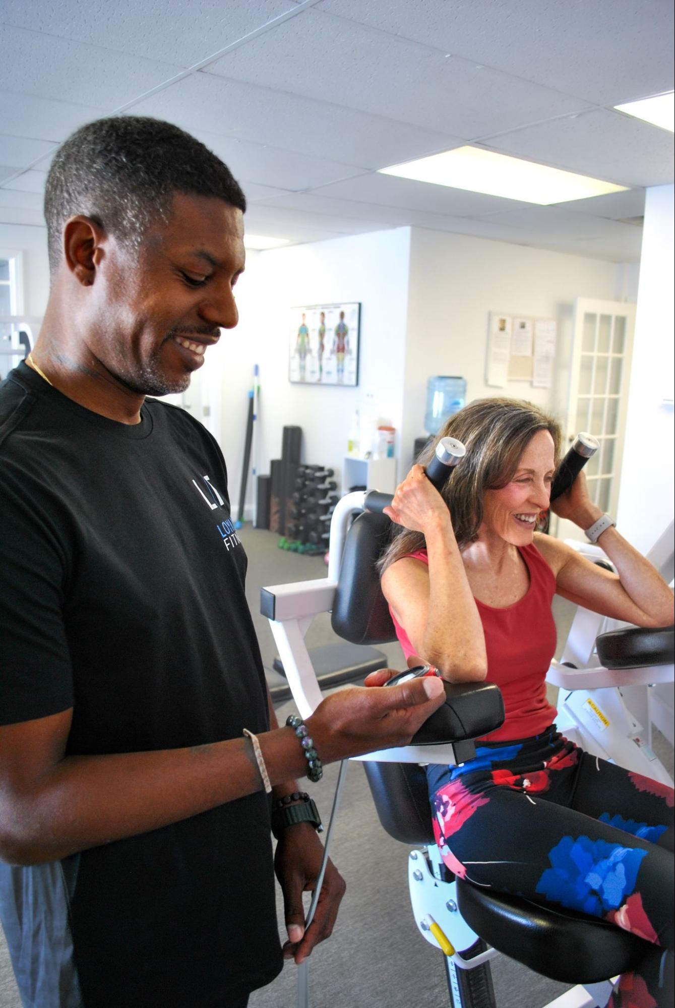 Trainer holding a stopwatch while his client is working out on an exercise machine.