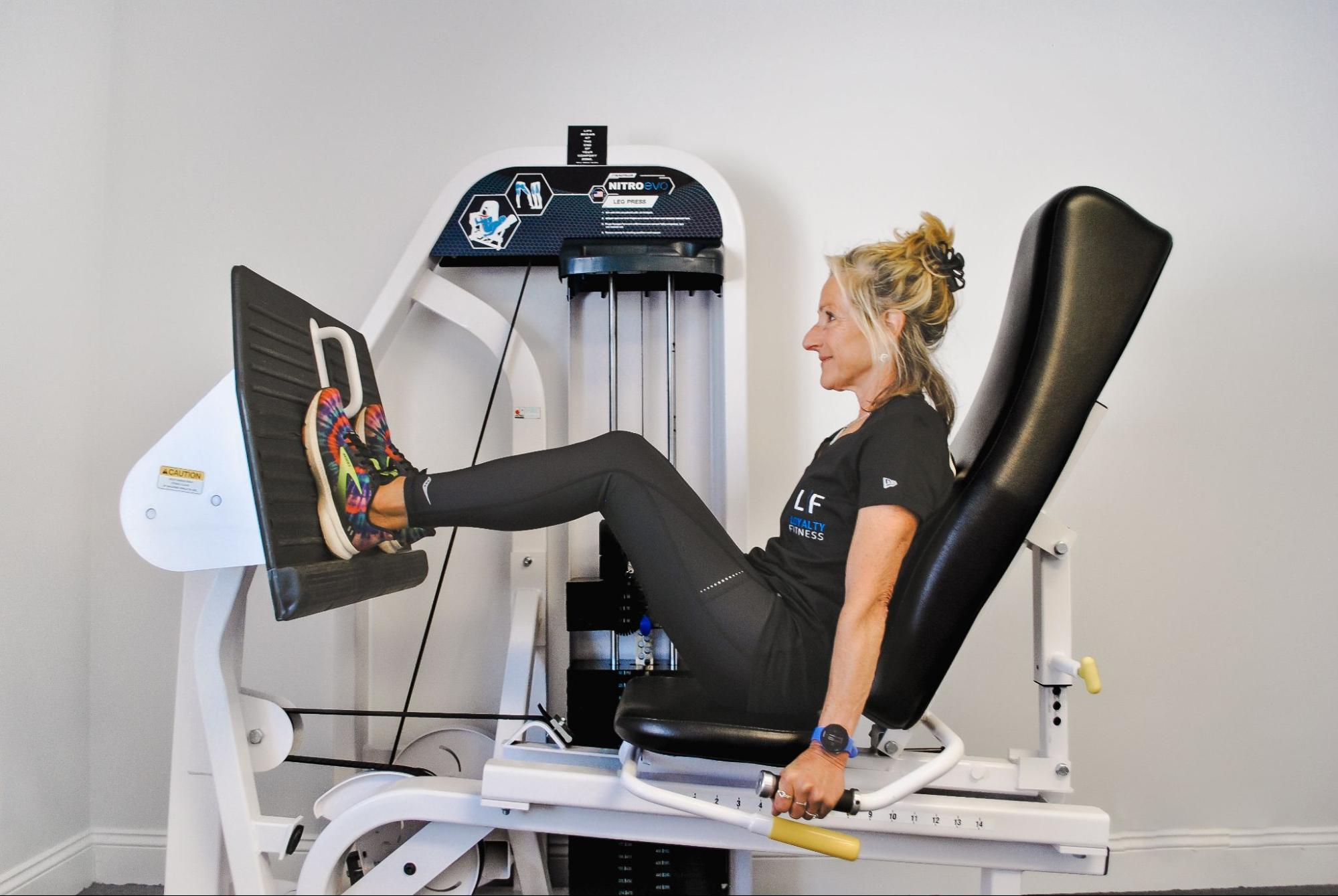 Woman working out on a leg press machine in an indoor gym.