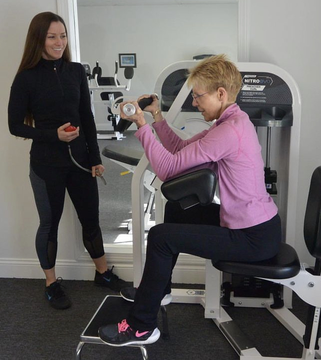 Woman training on an exercise machine while her trainer is watching her.