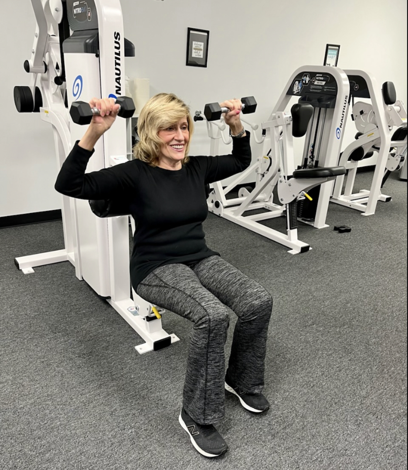 A Loyalty Fitness client lifting two dumbbells over her head at our Greenwich, CT location.